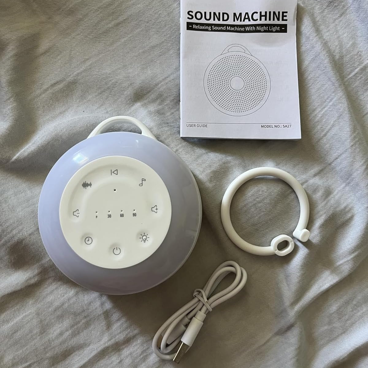 Sound machine with night light, packaging, and USB cable on a bed