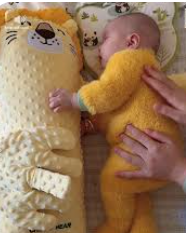 Baby in a yellow outfit lying on a soft pillow with a cartoon lion face