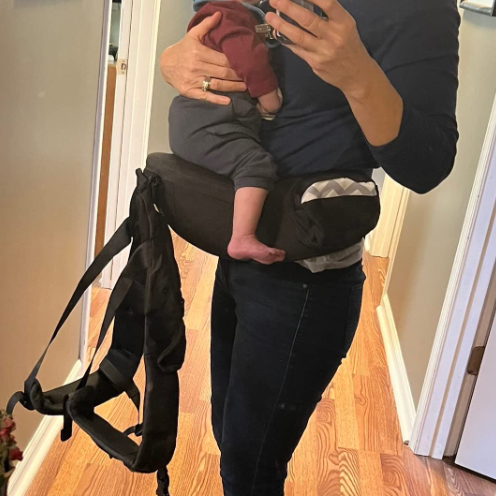Person holding a baby in a carrier with a wooden floor background