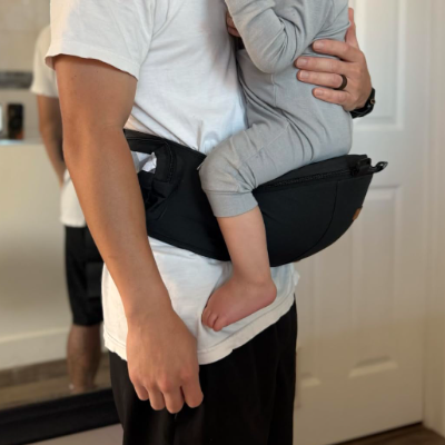 Person holding a child in a black baby carrier indoors.
