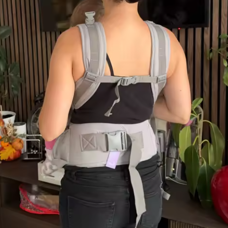 Person wearing a gray and black back brace in an indoor setting with plants and furniture.
