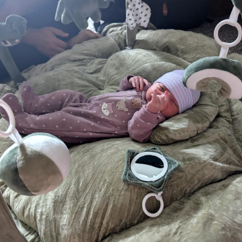 Newborn baby in a pink outfit lying on a green blanket with toys around