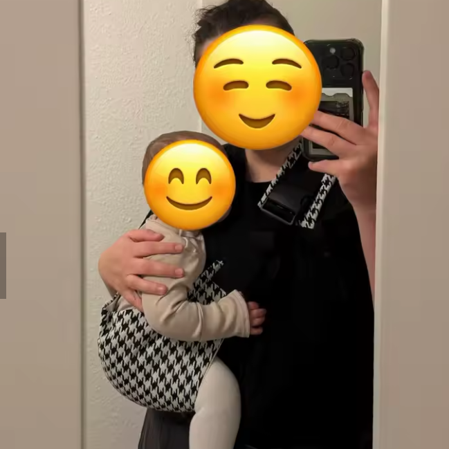 Person holding a child with emoji faces over their eyes, taking a mirror selfie.