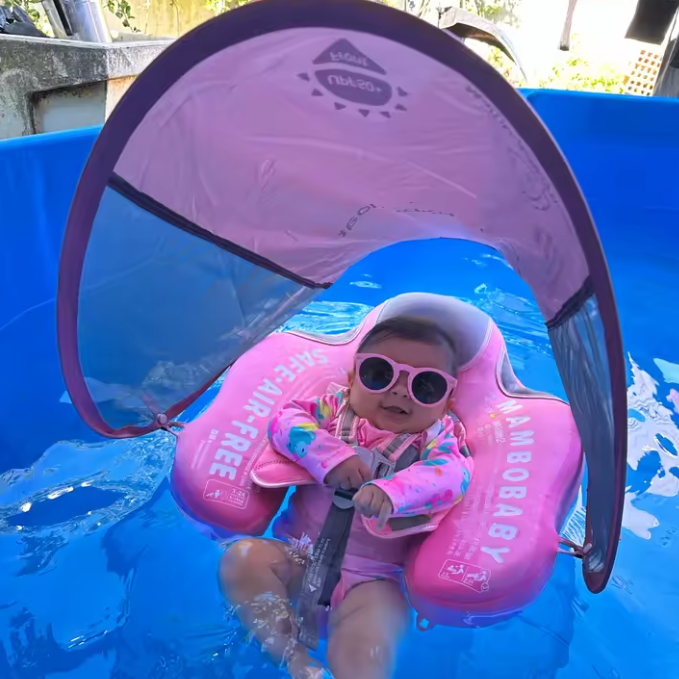 Child in a pink inflatable pool float with sunglasses and a canopy in a pool.