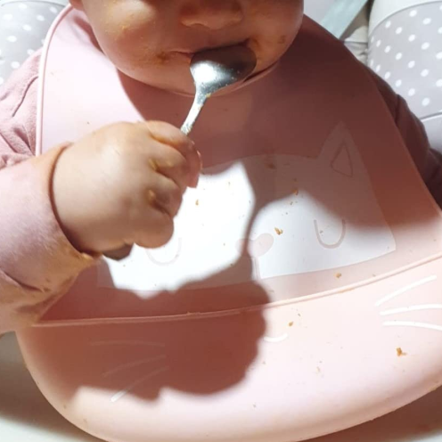 Baby eating with a spoon on a pink plate